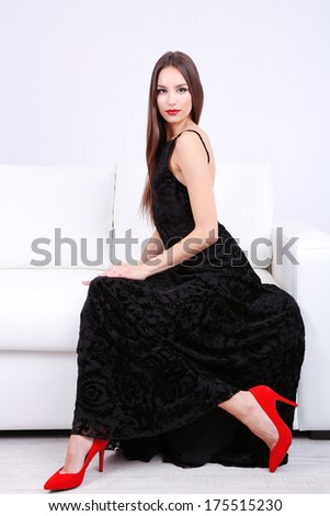 Beautiful young woman in black dress on sofa on white background