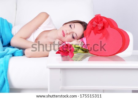 Beautiful young woman sleeping on sofa  near table with gifts and flowers, close up