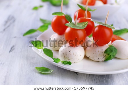 Tasty mozzarella cheese with basil and tomatoes on plate, on wooden table