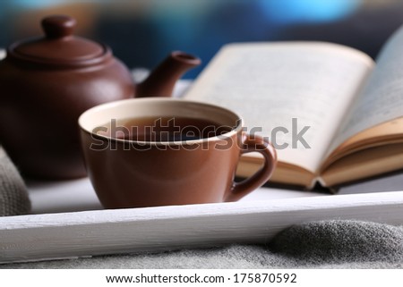Cup of hot tea with teapot and book on table on bright background