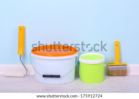 Paints, roll and paintbrush on floor in room on wall background