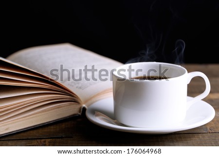 Cup of hot coffee with book on table on dark background