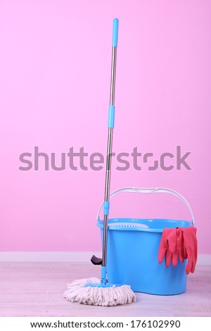 Floor mop and bucket for washing in room on pink wall background