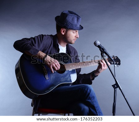 Young musician playing acoustic guitar and singing, on gray background