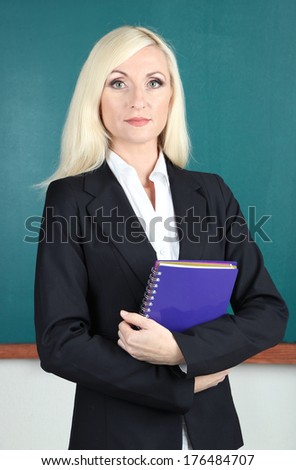 School teacher near blackboard with exercise book in classroom
