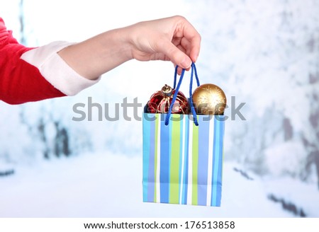 Hand holds package with New Year balls on snow background