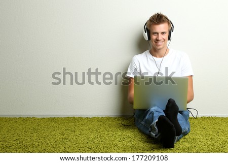 Young man relaxing on carpet and listening to music, on gray wall background