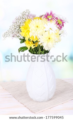 Beautiful chrysanthemum flowers in vase on table on light background