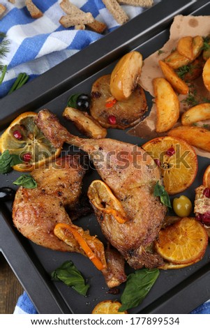 Homemade roasted chicken drumsticks with fried potatoes and vegetables on pan, on wooden background