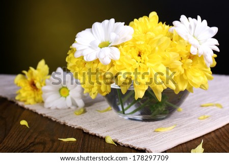 Beautiful chrysanthemum flowers in vase on table on dark yellow background