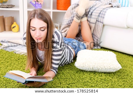 Young woman resting with book on fluffy carpet, near sofa at home