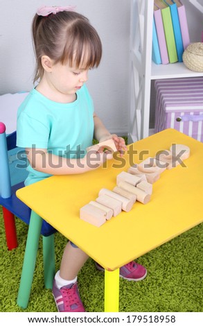 Little girl plays with construction blocks sitting at table in room