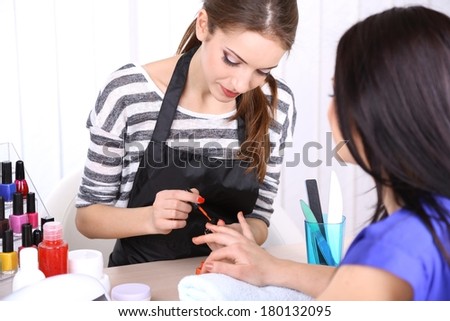 Beautiful girl manicurist doing manicure for woman in beauty salon