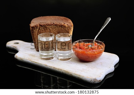 Composition with glass of vodka, red caviar, fresh bread on wooden board,  isolated on black