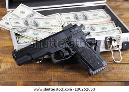 Case with money and gun, on wooden background
