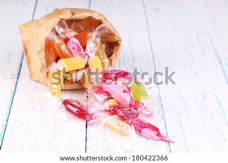 Tasty candies in paper bag on wooden background
