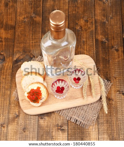 Composition with bottle of vodka  bread and red caviar on wooden table, on bright background