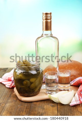 Composition with bottle of vodka and marinated vegetables on wooden table, on bright background