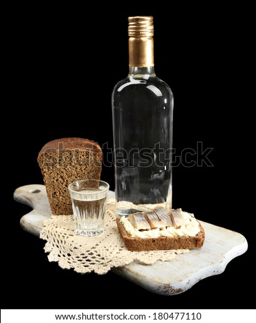 Bottle of vodka, sandwich with salted fish and glasses on wooden board, isolated on black