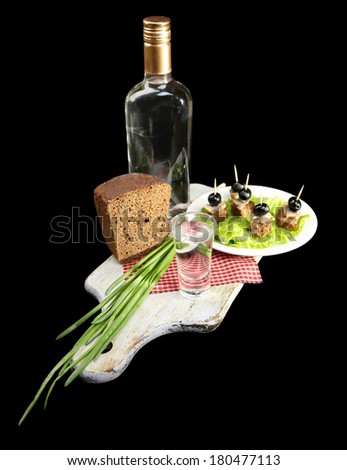 Composition with bottle of vodka, snacks with salted fish, green onion and glass on wooden board, isolated on black