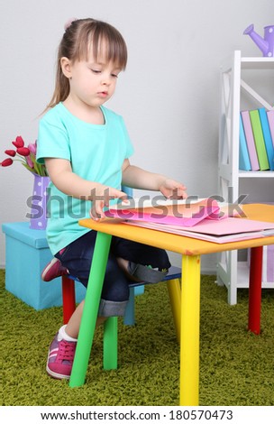 Little girl reads book sitting at table in room