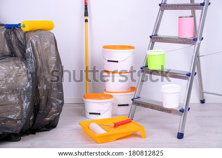 Buckets with paint, wrapped sofa and ladder on wall background. Conceptual photo of repairing works in  room