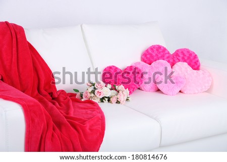 Pink hearts shaped pillows and flowers on white sofa