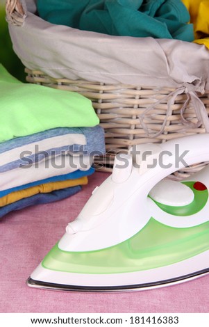 Iron and pile of colorful clothes and basket on table close up