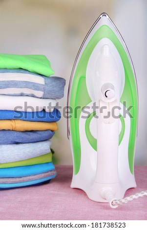 Iron and pile of colorful clothes on table on bright background