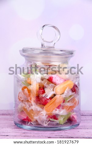 Tasty candies in jar on table on bright background