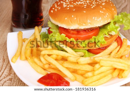 Big and tasty hamburger and fried potatoes on plate with cola close-up on wooden table