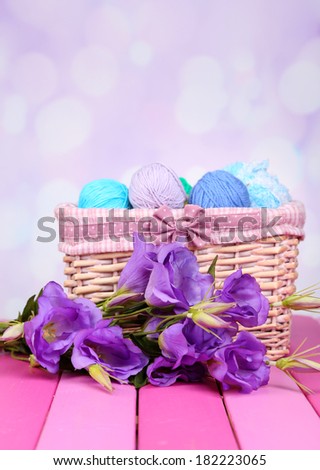 Purple artificial eustoma and woolen balls of yarn in basket on light background