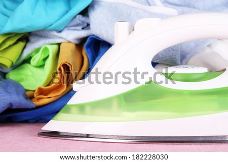 Iron and pile of colorful clothes  on table close up