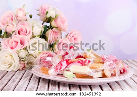 Tasty candies on plate with flowers on table on bright background