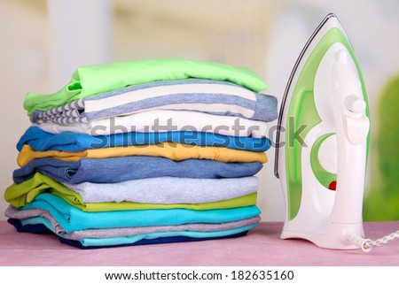Iron and pile of colorful clothes on table on bright background