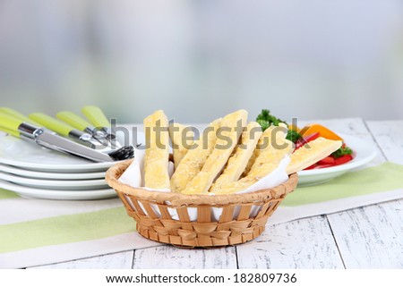Bread sticks  in wicker basket on wooden table on light background