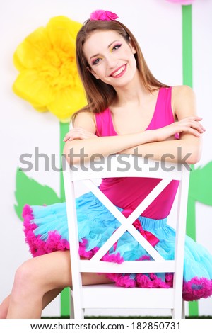 Beautiful young woman in petty skirt sitting on chair on decorative background