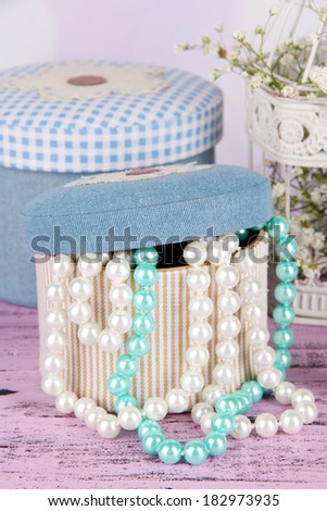 Decorative boxes with beads and flowers on table on bright background