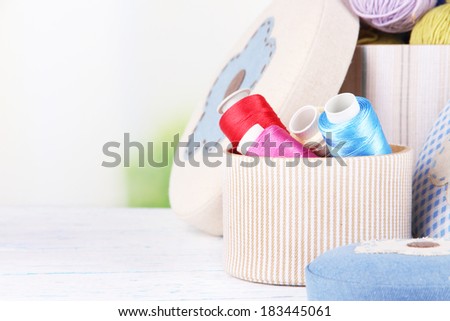 Decorative boxes with colorful skeins of thread on table on bright background