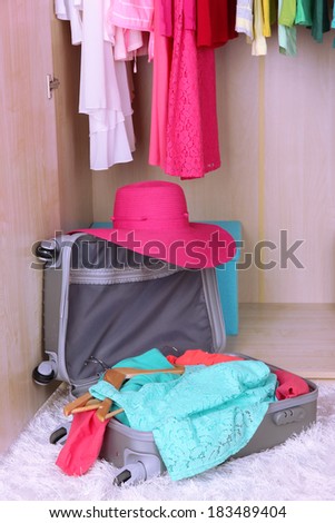 Female clothes in wardrobe and suitcase in room