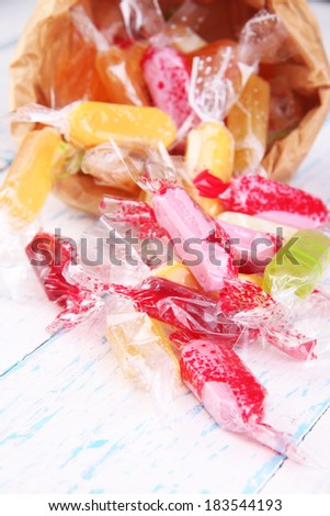 Tasty candies in paper bag on wooden background