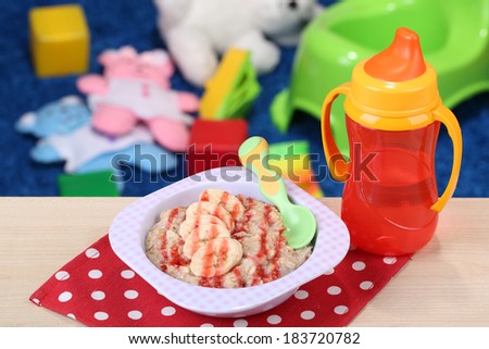 Bowl of porridge for baby and toys  on table, on toys background