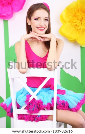Beautiful young woman in petty skirt sitting on chair on decorative background