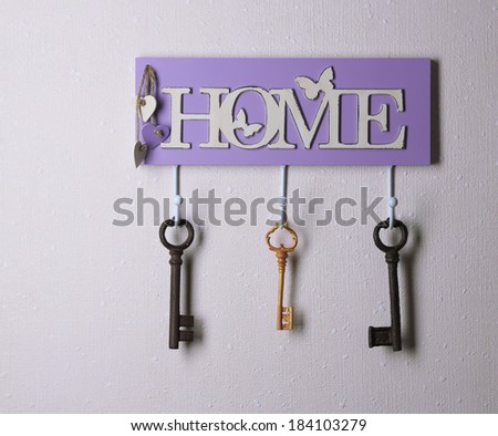 Old keys hanging from hooks, on light wall background