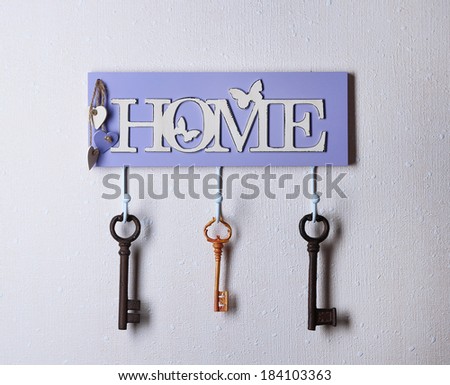 Old keys hanging from hooks, on light wall background