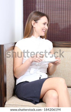 Young businesswoman sitting on couch and drinking coffee in office