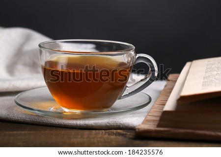 Cup of hot tea with book on table on dark background
