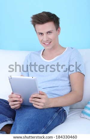 Guy sitting on sofa with electronic tablet on blue background