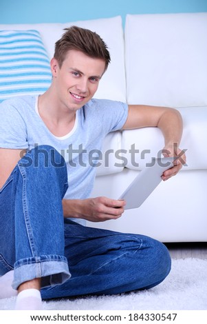 Guy sitting on floor with electronic tablet on room  background