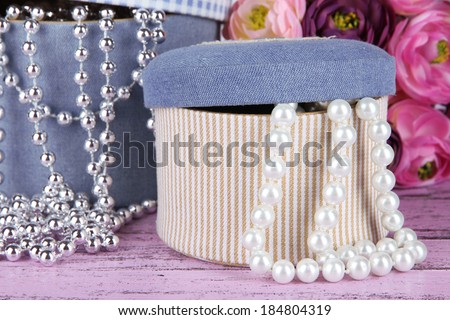 Decorative boxes with beads and flowers on wooden background